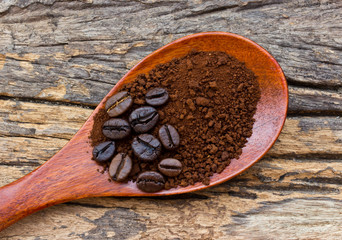 Roasted coffee beans and ground coffee in wooden spoon on textur