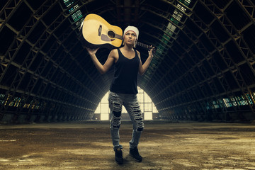 Young woman posing with acoustic guitar in abandoned factory