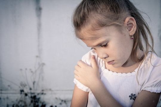 Portrait of sad little girl sitting near  wall in the day time