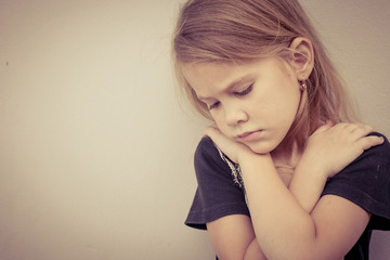 Portrait of sad little girl sitting near  wall in the day time