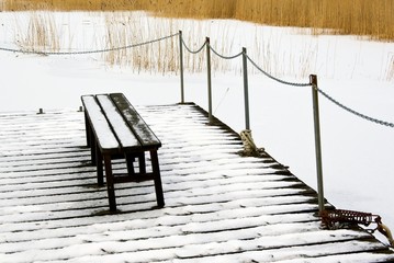 Bench on snowy bridge and frozen sea in winter.