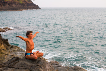 Young man doing yoga exercise on sea beach.