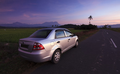 Fototapeta na wymiar Car parked on roadside in a rural area at sunset