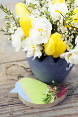 Bouquet of tulips and daffodils in vase on wooden background