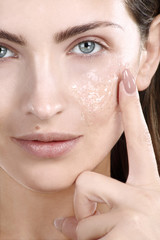 Beautiful woman applying scrub treatment on face