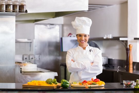Smiling female chef with cut vegetables in kitchen