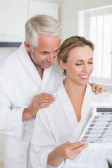 Obraz premium Happy couple reading newspaper together in bathrobes