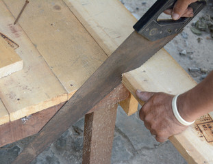 carpenter cutting a slat of wood using a saw 