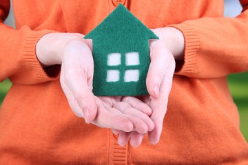 Little paper house in hand close-up, on bright background