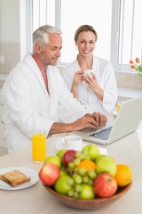 Smiling couple using laptop at breakfast in bathrobes