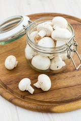 Fresh mushrooms in a glass jar on a wooden surface