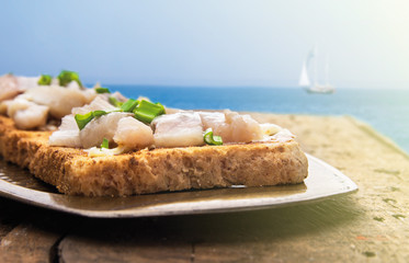 toast with salted herring,wooden table, blue sea and sky