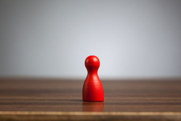 Red pawn figure toy, table, grey background.