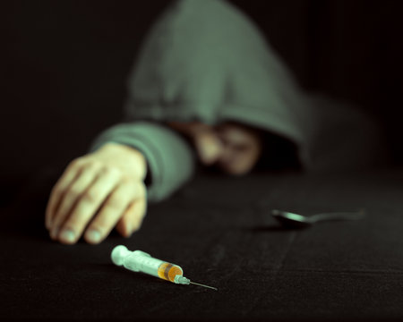 Grunge image of a depressed drug addict looking at a syringe