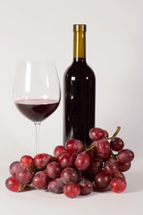 Calice di vino con bottiglia e uva rossa isolato su bianco