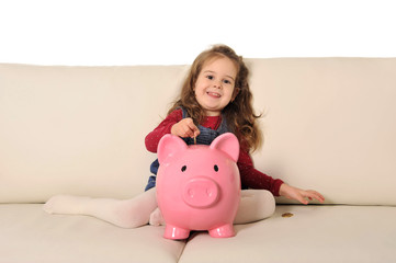 Cute little girl playing puts coin in huge piggy bank on sofa