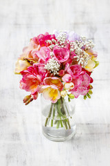 Bouquet of colorful freesia flowers in transparent glass vase.