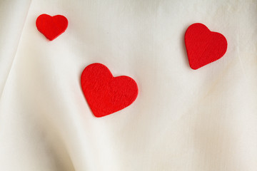 Red wooden decorative hearts on white silk background.