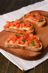 Delicious bruschetta with tomatoes on cutting board close-up