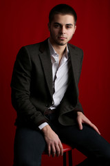 Handsome young sitting on chair on red background