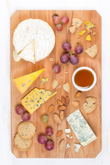 assorted soft cheeses, grapes, nuts and honey on a cutting board