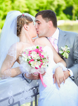 portrait of newly married couple kissing at park at sunny day