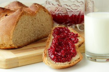 A slice of bread, spread with raspberry jam and a glass of milk