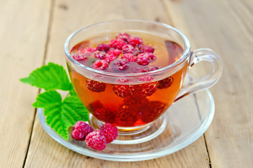 Tea with raspberry and leaf in a cup on board