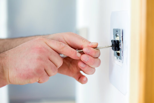 Man installing light switch with screwdriver 