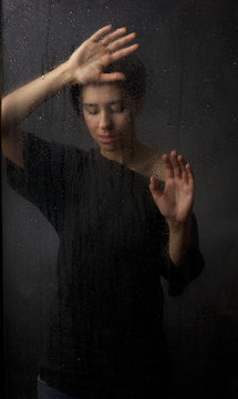 The girl behind the wet glass on a dark background.