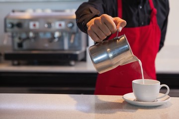Fototapeta na wymiar Barista pouring milk into cup of coffee