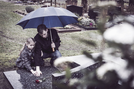 Father and daughter visiting grave of deceased mother