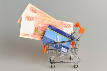 Credit card and money within shopping cart on gray