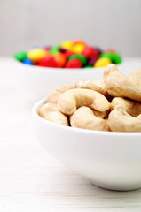 Cashew nuts in a white bowl and colorful candies in the backgrou
