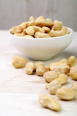 Cashew nuts in a white bowl and some scattered around
