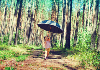 Happy little girl hiding under big black umbrella in fair weathe