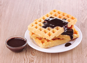 Tasty waffles with chocolate on plate on wooden background