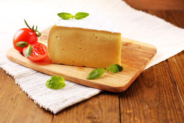 Tasty Camembert cheese with tomato and basil, on wooden table