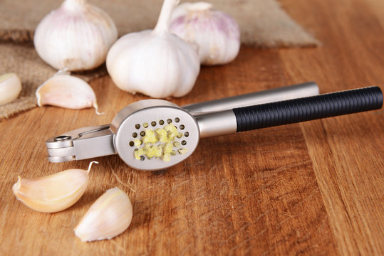 Garlic press with garlic on wooden background
