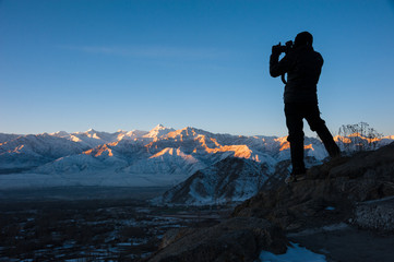 Silhouette of traveler taking photo of sunrise over mountain.