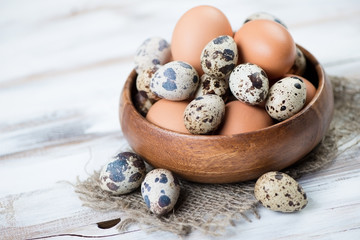 Wooden bowl with raw quail and chicken eggs