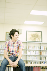 Fototapeta premium smiling male student sitting on bookshelf