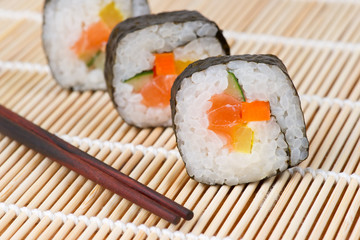 sushi with salmon and cucumber on bamboo mat with chopsticks