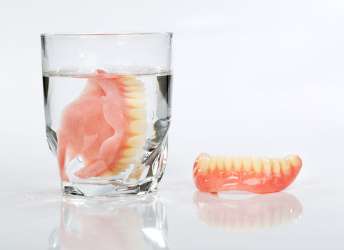 A set of dentures in a glass of water on a white background
