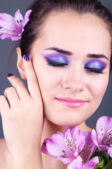 Beautiful young woman with flowers on gray background