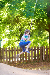 Naklejka na ściany i meble Funny little boy enjoying a swing ride on a playground