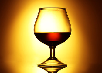Glass of cognac on yellow background