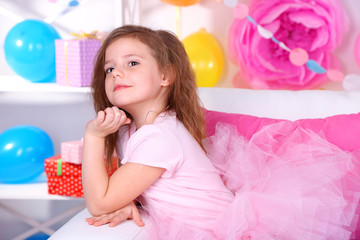Pretty little girl sitting on sofa on celebratory background