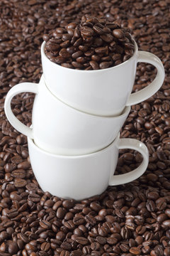 Drei Kaffeetassen gestaplet stehen zwischen Kaffeebohnen