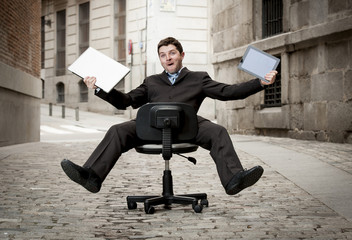 business man rolling downhill on chair with computer and tablet